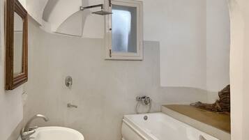 A bathroom with a white sink, a bathtub, a window, and a mirror.