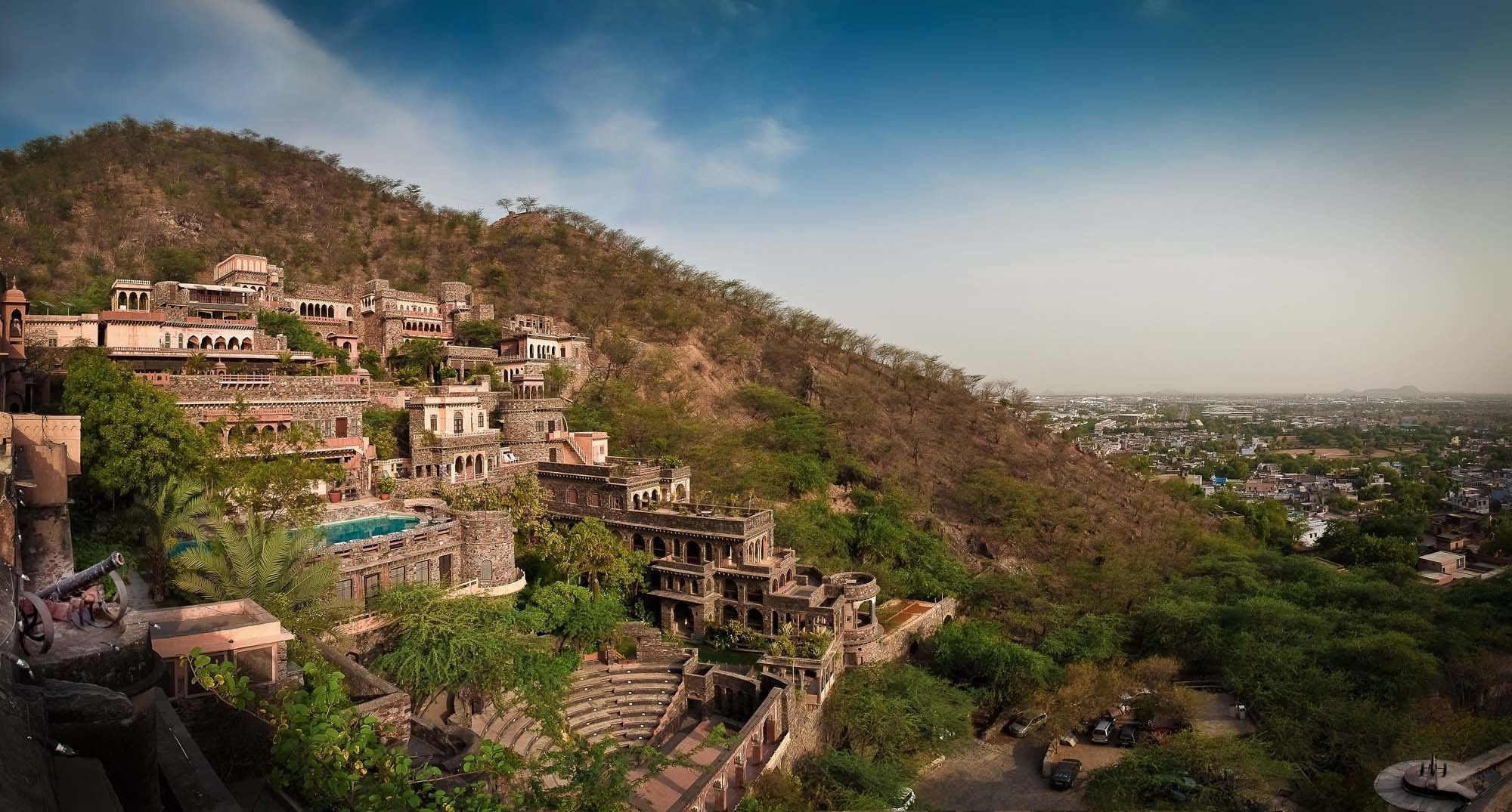 A historic hilltop complex with ancient architecture, including a large courtyard and a small pool.