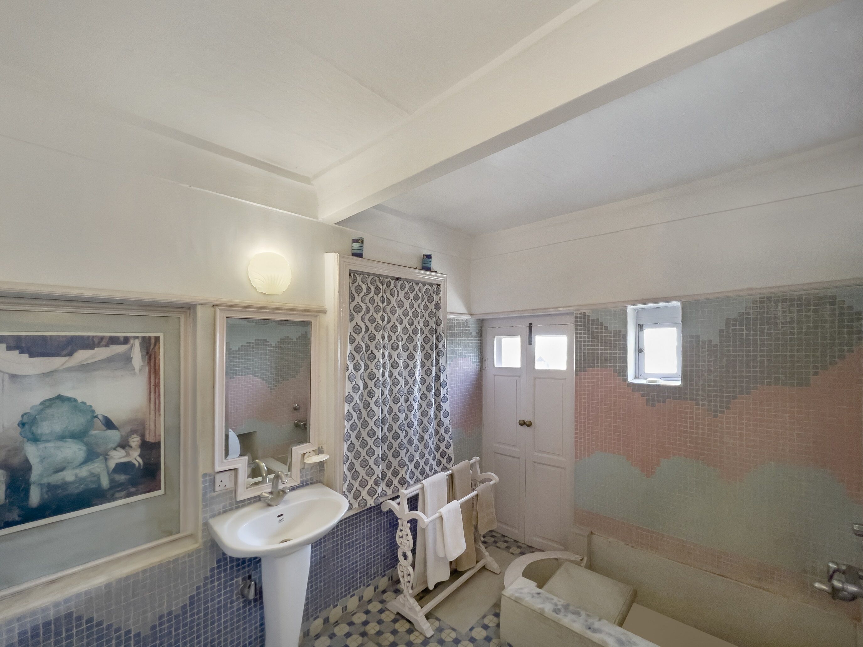 Ein Badezimmer mit weißem Waschbecken, einem Spiegel, einer Dusche mit weißer Badewanne und einer gefliesten Wand.