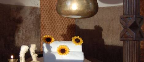 A shelf with a brass pot, a white cloth, and sunflowers.