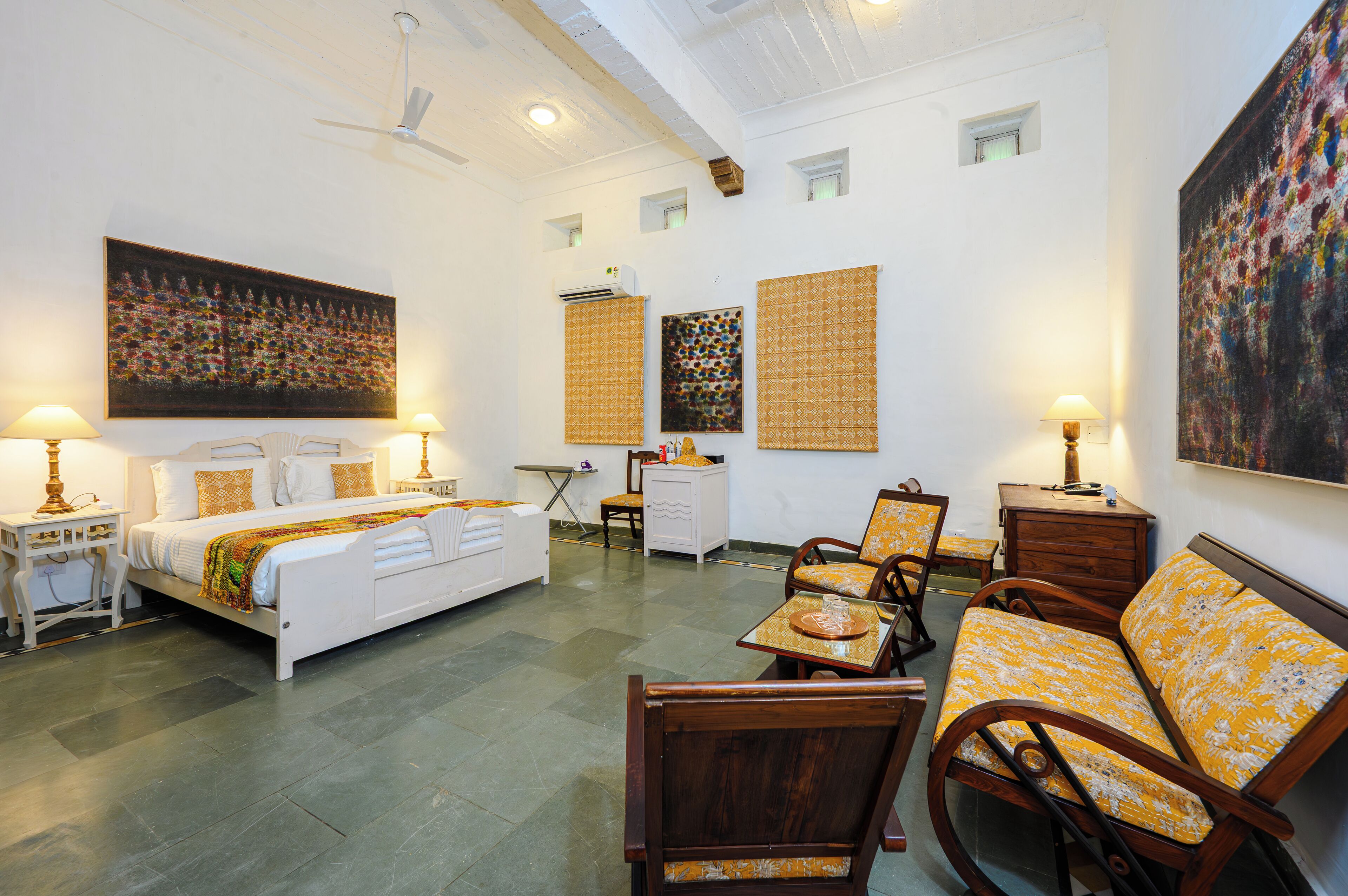 A hotel room with a bed, two chairs, a small table, a desk, and artwork on the walls.