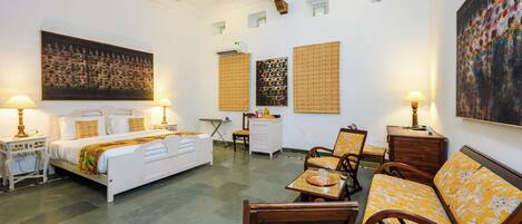 A hotel room with a bed, two chairs, a small table, a desk, and artwork on the walls.