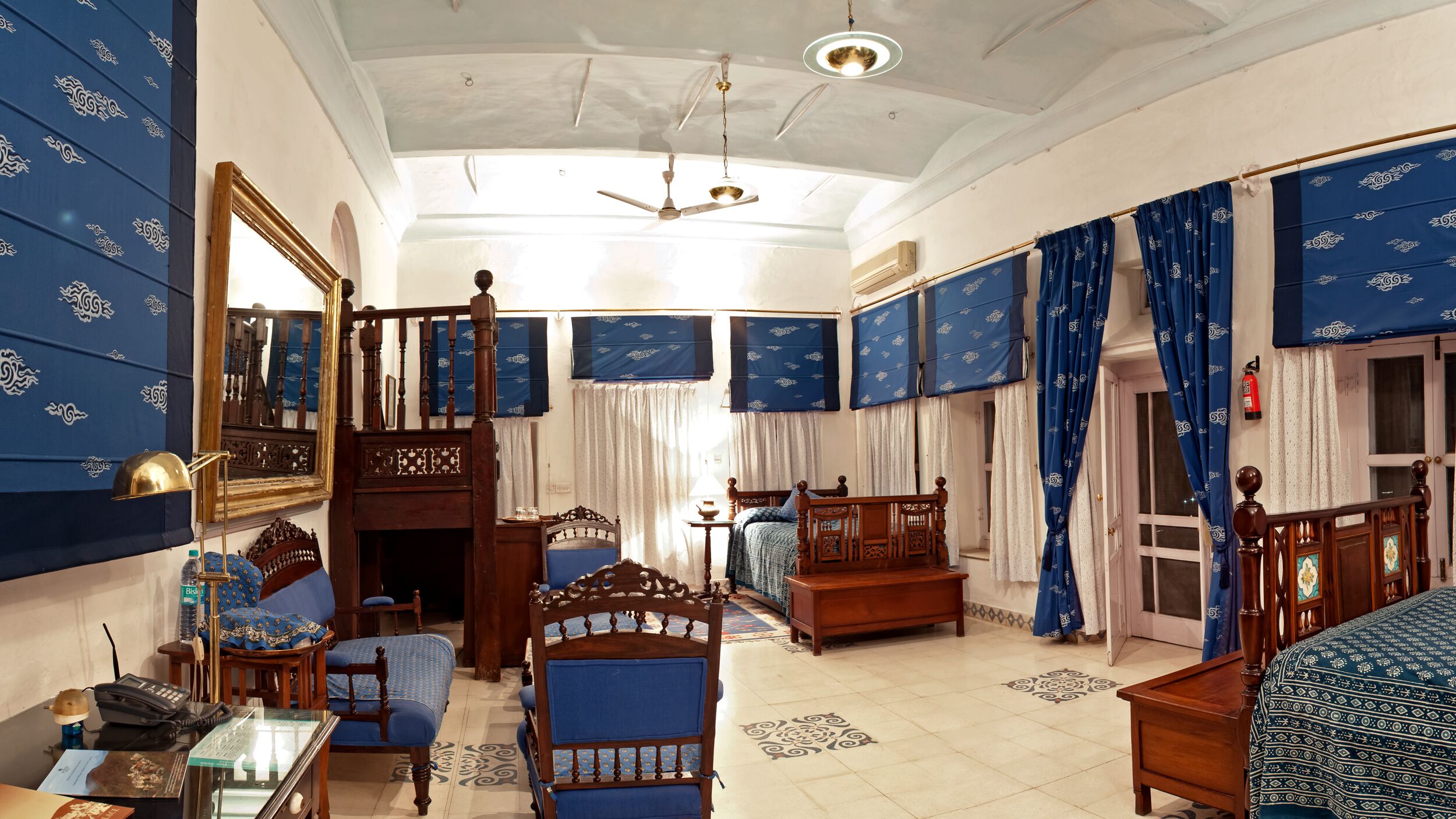 Una habitación tradicional con una cama y una silla de madera, una mesita pequeña y un ventilador de techo.