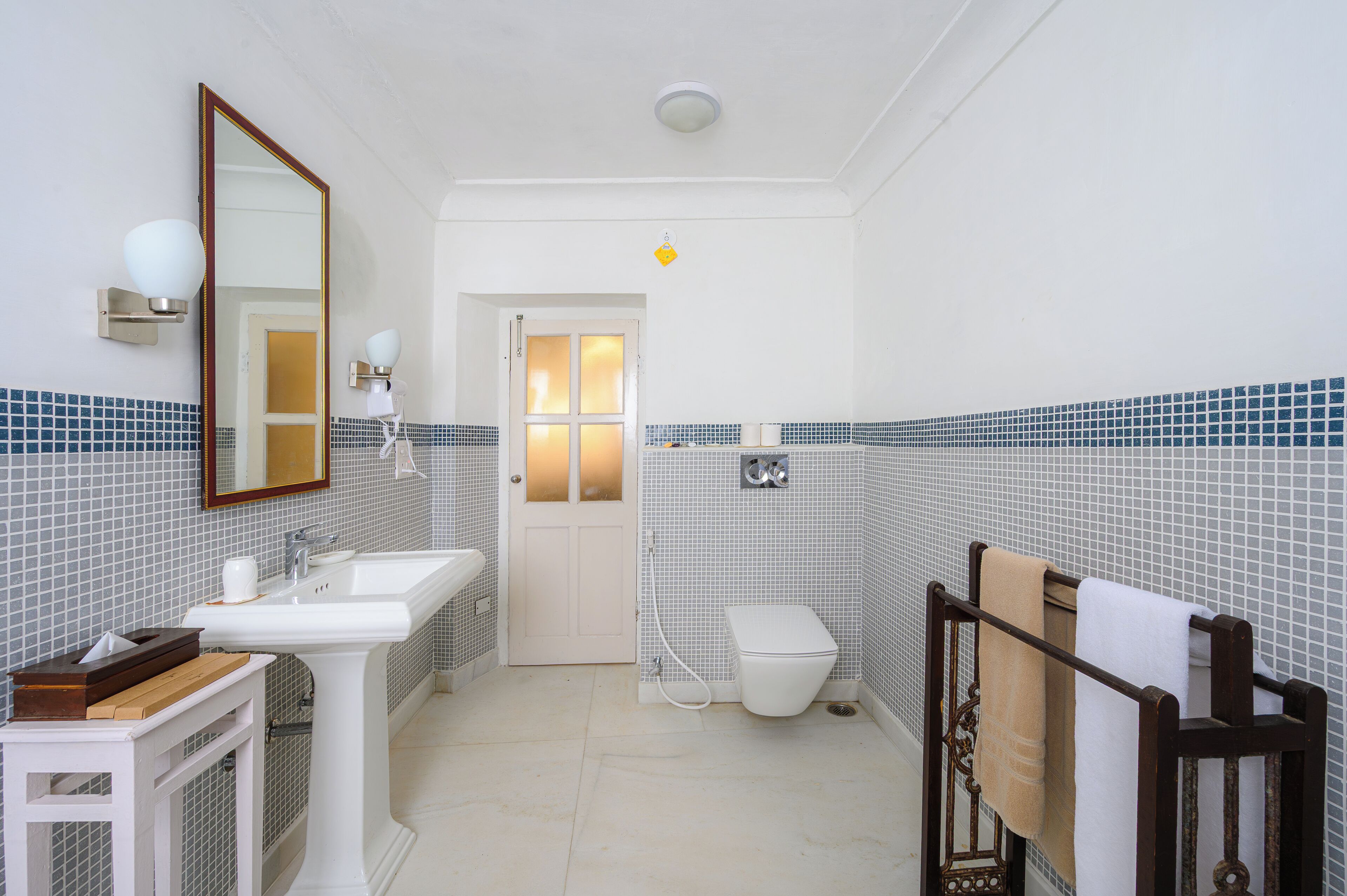A bathroom with a white sink, mirror, and toilet, tiled walls, and a towel rack.