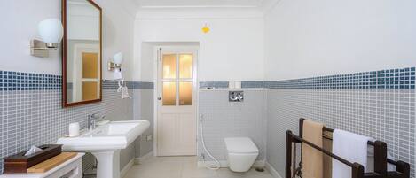 A bathroom with a white sink, mirror, and toilet, tiled walls, and a towel rack.