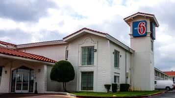 Un motel con un llamativo letrero con el número '6', una entrada con puerta de rejas y un área de estacionamiento.