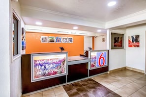 A reception desk with a sign that reads 'We'll leave the light on for you.' - Motel 6 Euless, TX - DFW West (Euless)