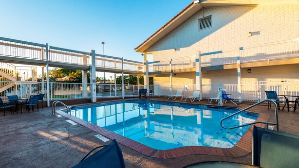 A pool area with lounge chairs, a covered walkway, and a building with multiple balconies. - Motel 6 Euless, TX - DFW West (Euless)