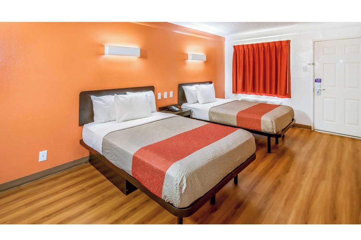 A hotel room with two beds, wooden flooring, and a door with a lock.