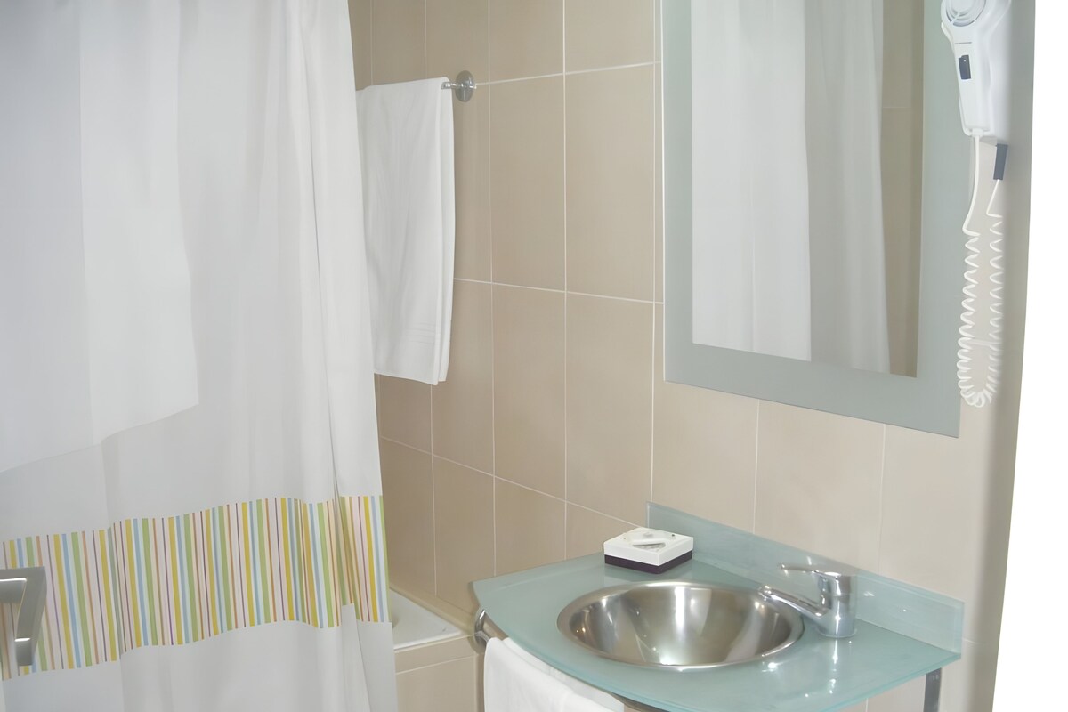 Un baño con un lavabo de cristal, un perchero, una cortina de ducha y un secador de pelo.