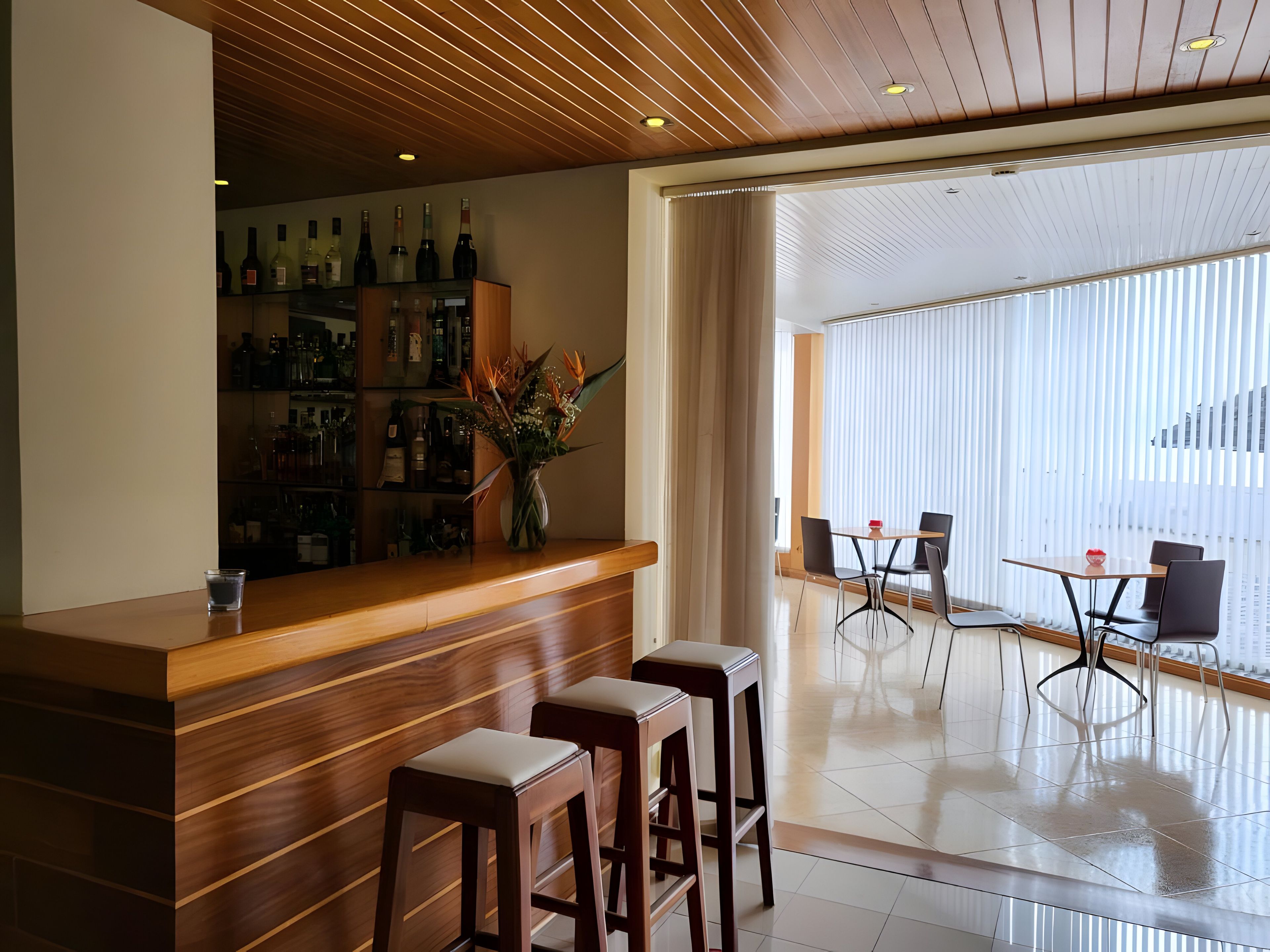 A bar area with a wooden counter, stools, and a variety of bottles.