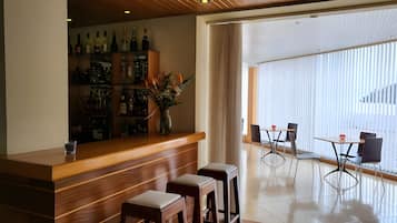 A bar area with a wooden counter, stools, and a variety of bottles.
