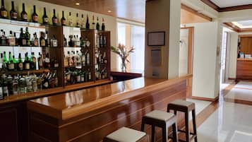 A bar area with wooden shelves stocked with various liquor bottles, a polished wooden counter, and two bar stools.