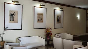 A modern living room with white furniture, framed artwork on the walls, and a small table with a vase of flowers.