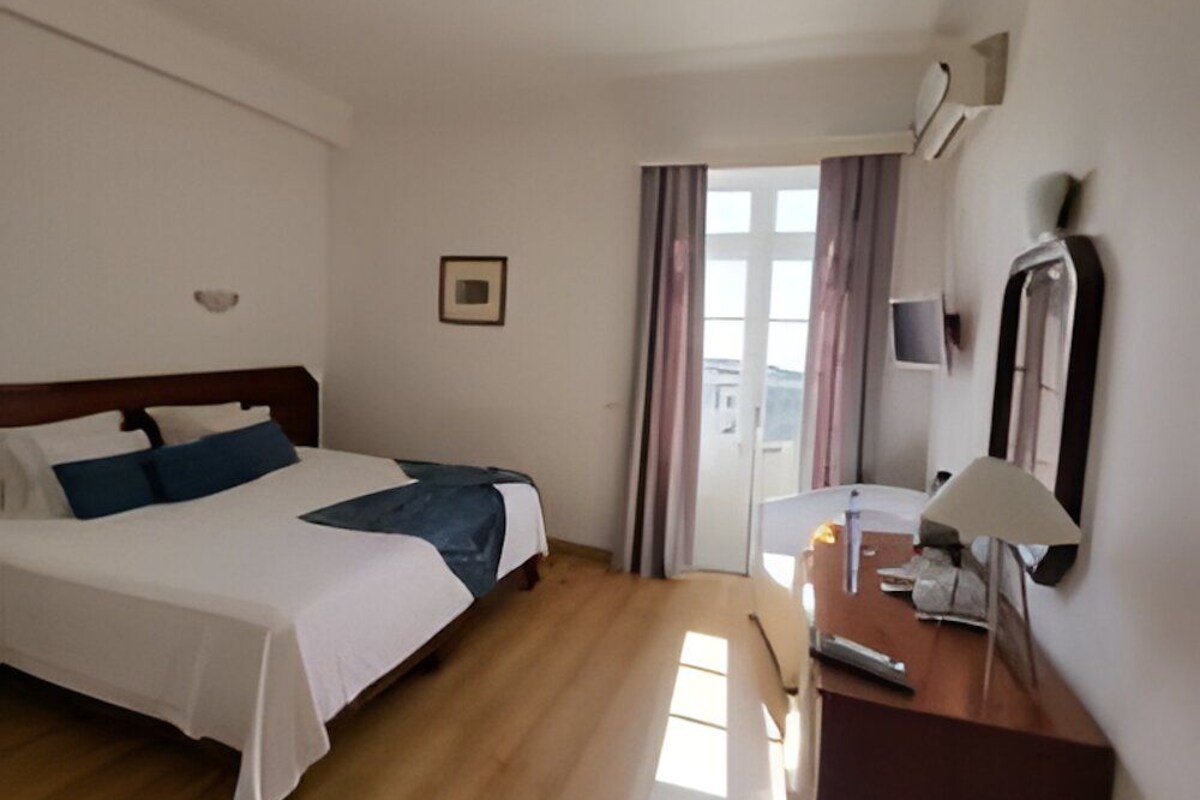 Habitación de hotel con cama, escritorio, silla, lámpara, espejo y ventana con cortinas.
