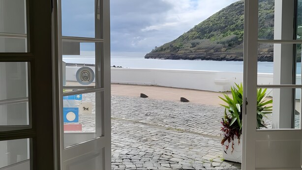 An open door leading to a beach with a view of the sea and a hill.