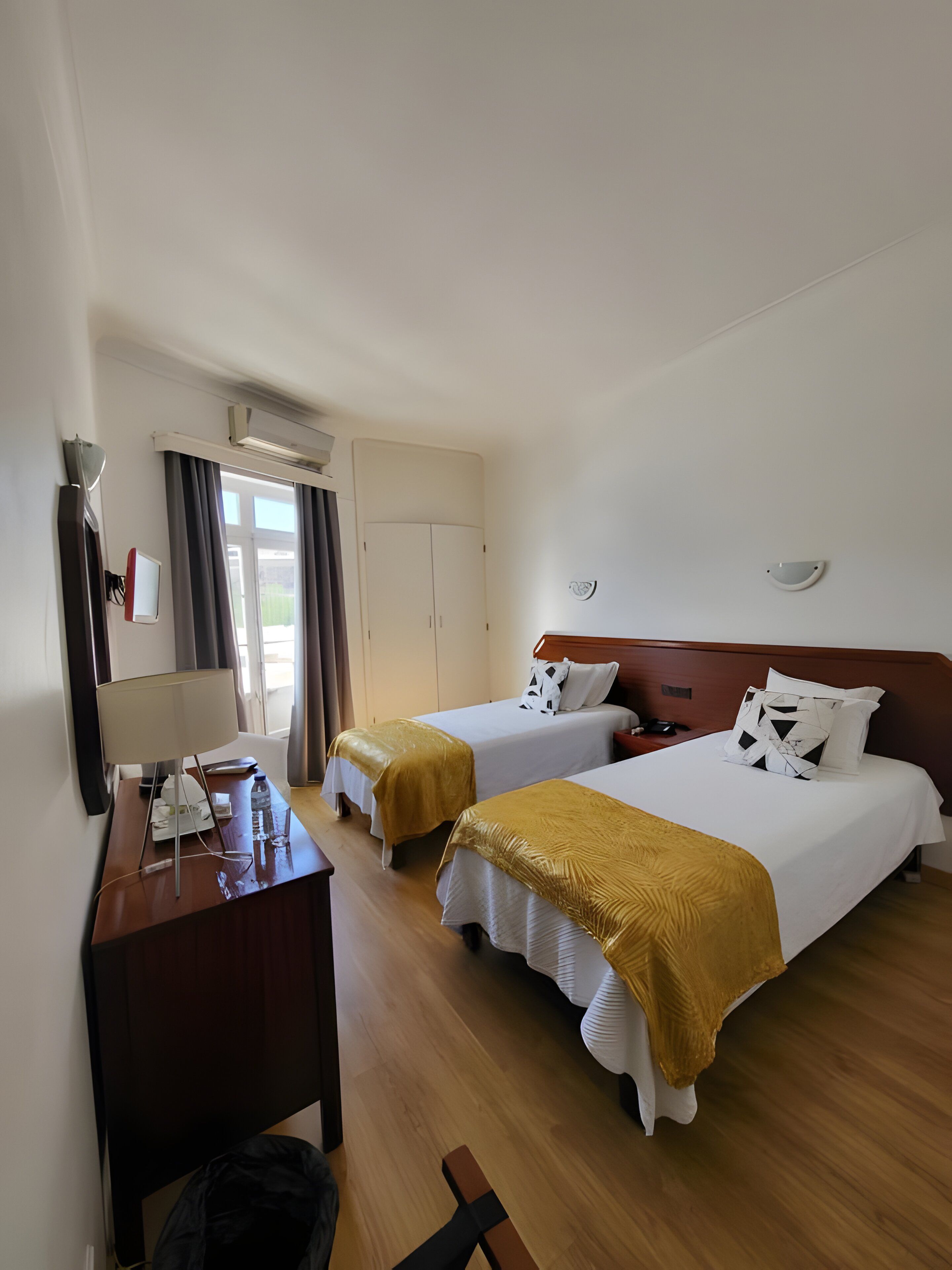 A hotel room with two beds, a desk with a lamp, a chair, and a wardrobe.