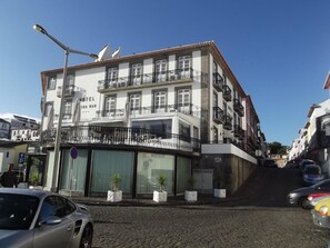 Un hotel de varios pisos con balcones, una señal de estacionamiento y una calle adoquinada.