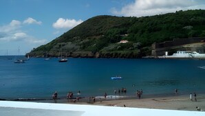 A coastal scene with a beach, boats, and a hill with buildings.