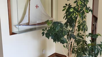 A corner room with a large mirror reflecting a sailboat, a potted plant, and a wooden floor.