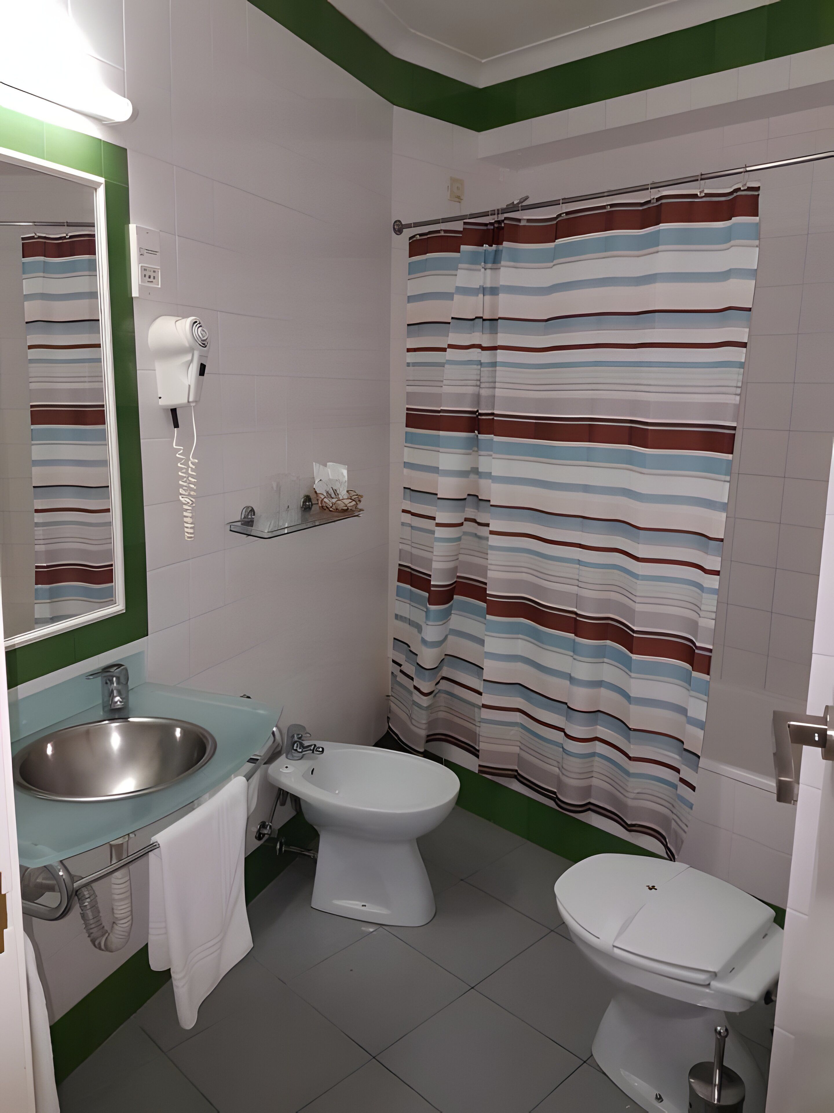 A bathroom with a sink, bidet, toilet, and a striped shower curtain.