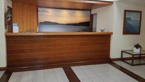 A reception desk with a wooden finish, a framed landscape painting, and a small table with a plant.