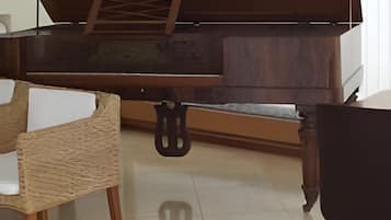 Un piano con detalles de madera, una silla tejida, una silla negra y un suelo de baldosas.