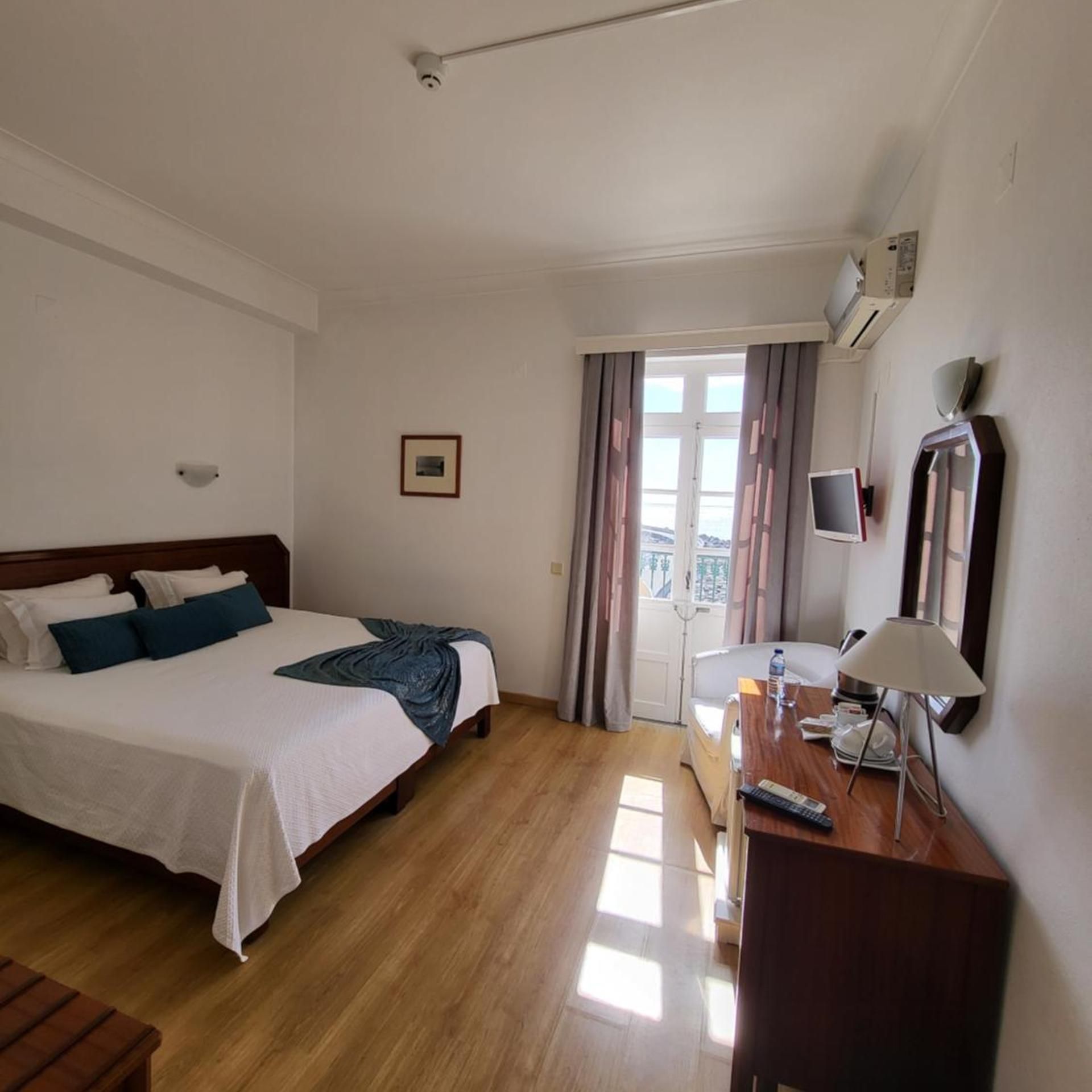 A hotel room with a bed, a desk, a chair, a TV, and a window with curtains.