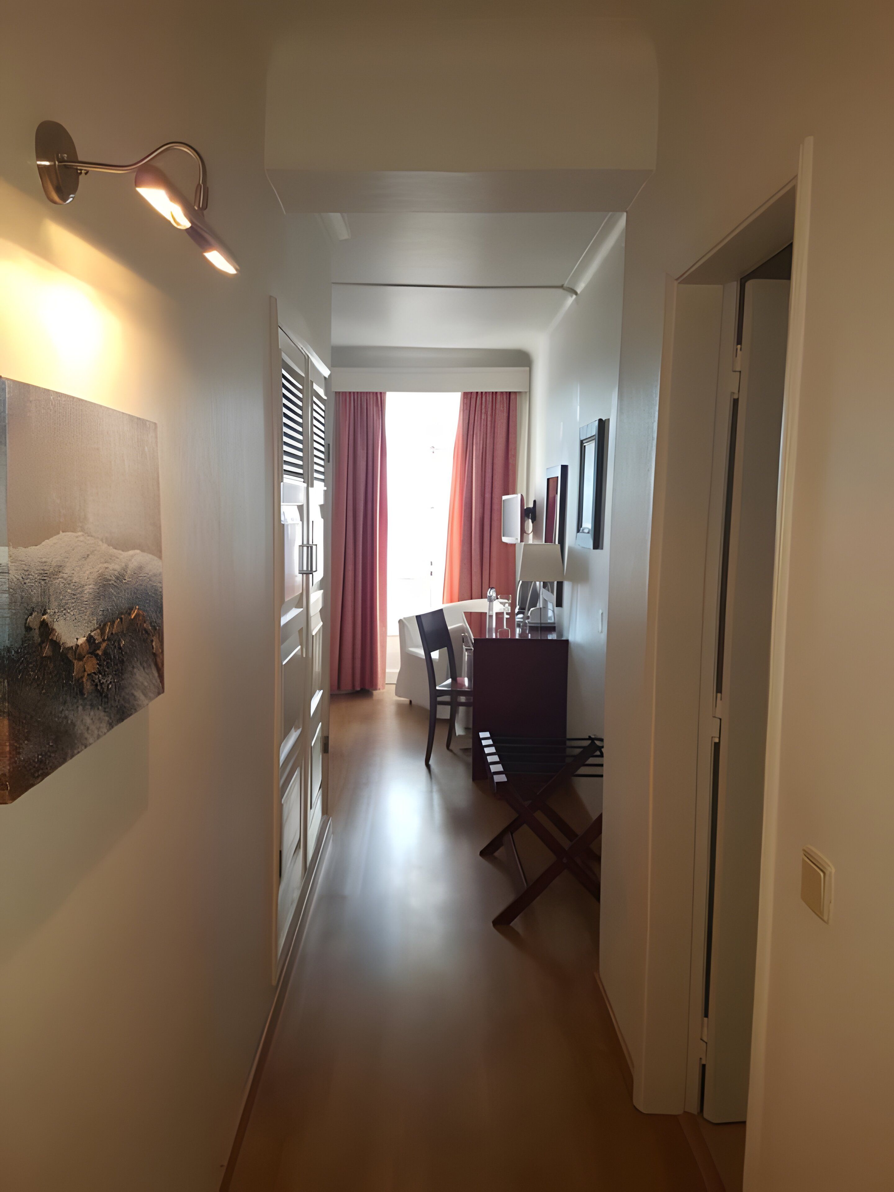A hallway leading to a dining area with a table and chairs, a painting on the wall, and a door on the right.