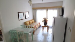 Uma sala de jantar com mesa, cadeiras, sofá, geladeira e ventilador de teto.