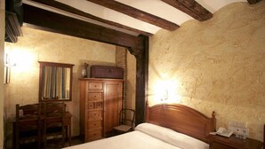 Une chambre à coucher avec un lit en bois, une table de chevet avec un téléphone et une lampe, une commode en bois et une chaise.
