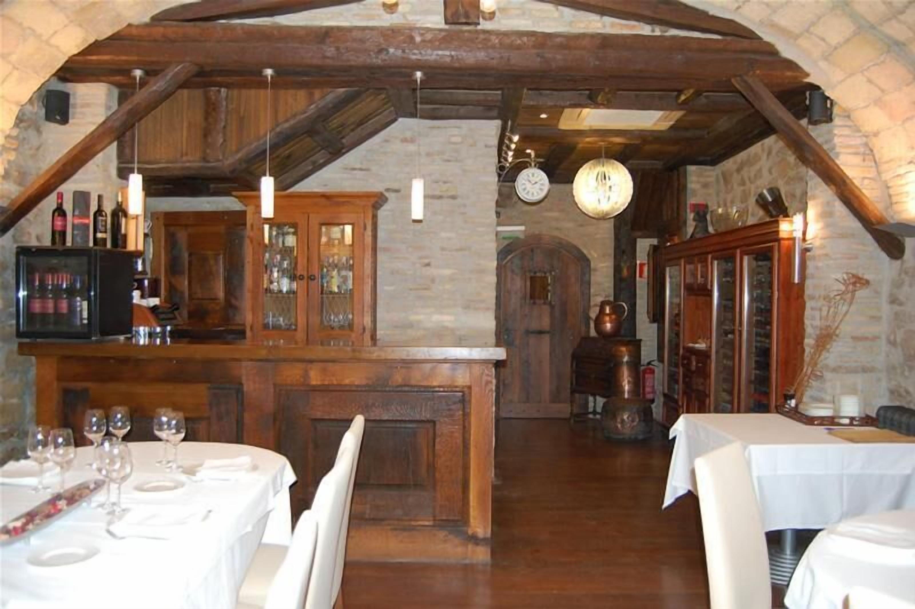 A rustic dining area with wooden beams, stone walls, and a bar with bottles and glasses.