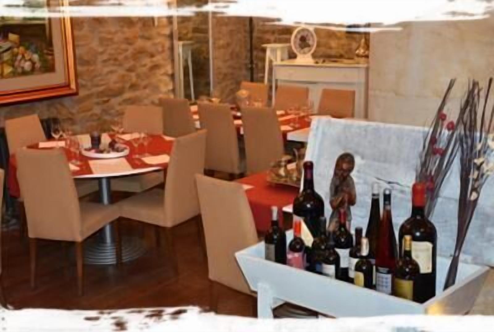 A dining area with multiple tables and chairs, a white tablecloth, and several wine bottles on a stand.