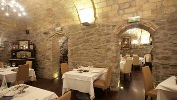 A restaurant with stone walls, tables set for dining, and a chandelier.