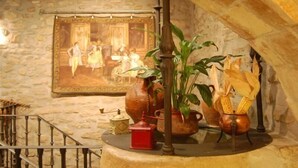 Une pièce rustique avec un mur en pierre, un tableau encadré, une grande plante et un pot en cuivre contenant du maïs.