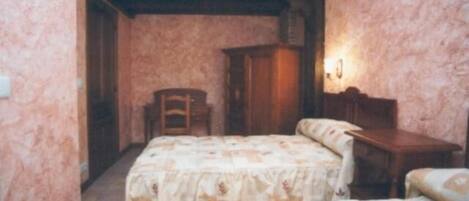 A bedroom with two beds, a wooden wardrobe, and a chair.