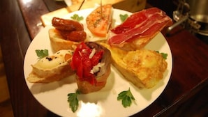 Une assiette d’amuse-gueules comprenant des bruschettas, du prosciutto et une pâtisserie farcie.