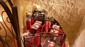 A restaurant with red upholstered chairs and tables, stone walls, and a staircase leading to a lower level.