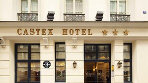 The facade of Castex Hotel with a signboard, three stars, and a black door.