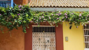 A traditional wooden door with a metal gate, a yellow wall, and a red wall with a blue balcony. - Hotel Casa Mejía (Cartagena)