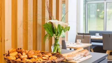 Un panier rempli de viennoiseries est posé sur un comptoir, avec un vase de fleurs et une vue sur la fenêtre en arrière-plan.