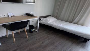 A small hotel room with a single bed, a desk with a chair, a telephone, and a television mounted on the wall.