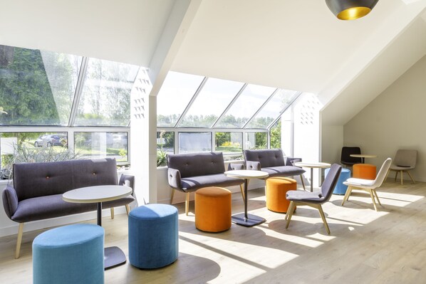 Un interior moderno con techo alto, ventanas amplias y una variedad de opciones de asientos, incluyendo sofás y sillones.