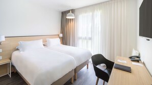 Een hotelkamer met twee bedden, een bureau met stoel, een lamp en een telefoon.