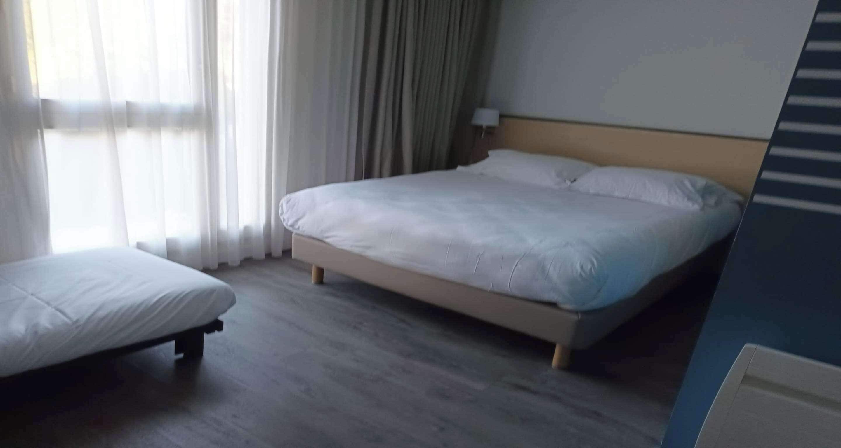 Een slaapkamer met een bed, nachtkastje en raam met gordijnen.