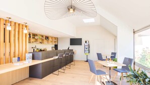 Een moderne bar met een houten toonbank, barstoelen en een grote hanglamp.