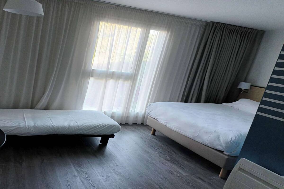 Een hotelkamer met twee eenpersoonsbedden, een bureau, een stoel en een raam met gordijnen.