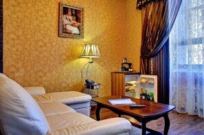 A room with a sofa, a table with a lamp, a painting on the wall, and a cabinet with bottles. - Hotel Astoria (Volgograd)
