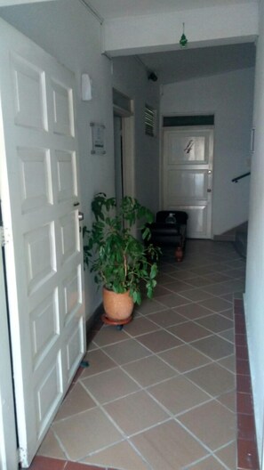 A hallway with a white door, a potted plant, and a black chair. - ARCO Apartasuites (Cali)