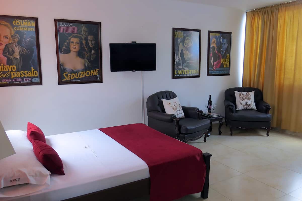 A hotel room with a bed, two armchairs, a TV, and movie posters on the wall.